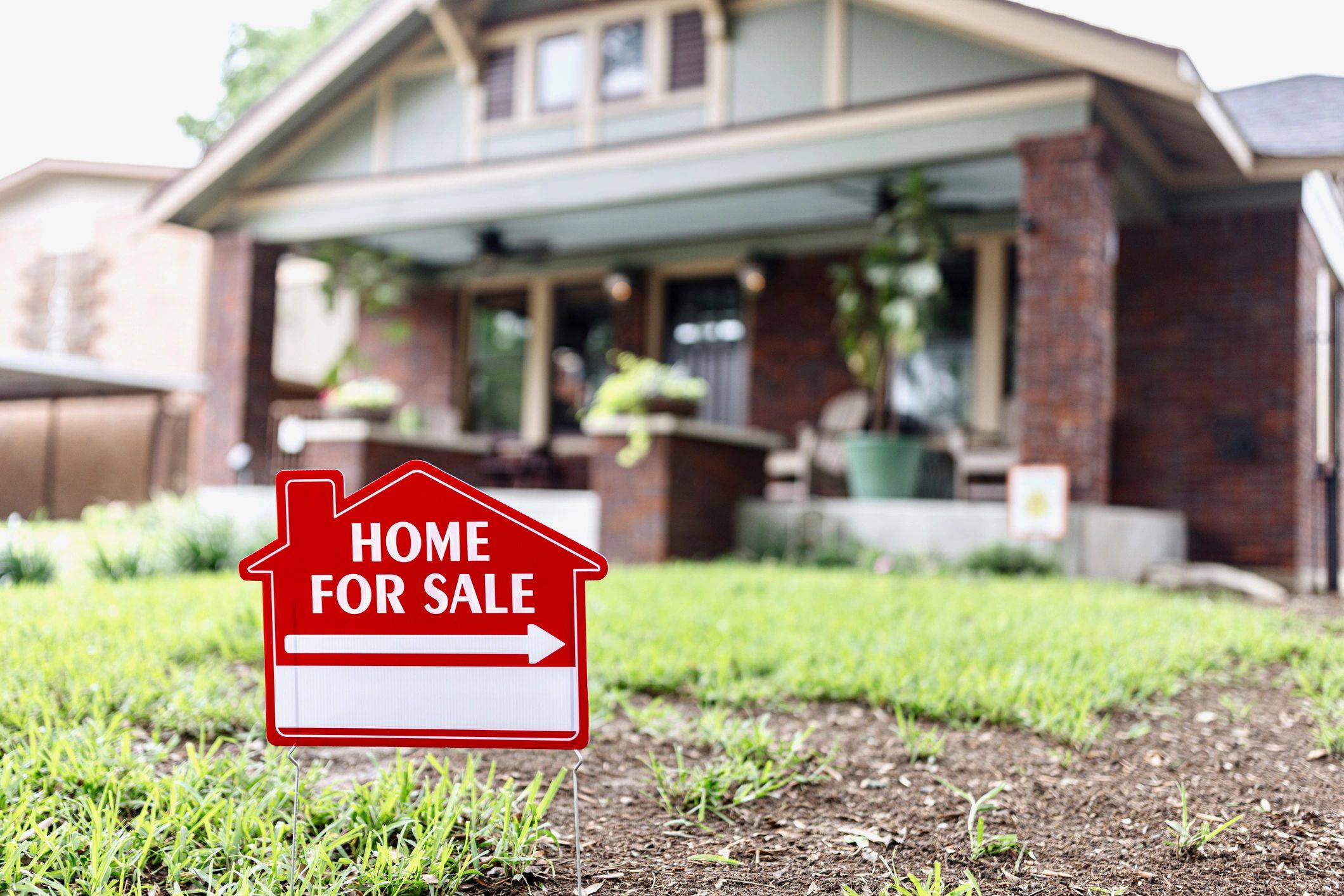 Home for sale yard sign in front of a brick bungalow house